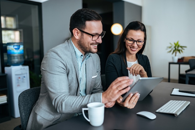 Dos hombres de negocios elegantes que sonríen y que miran la tableta digital.