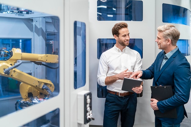 Dos hombres de negocios hablando en un robot en una fábrica moderna