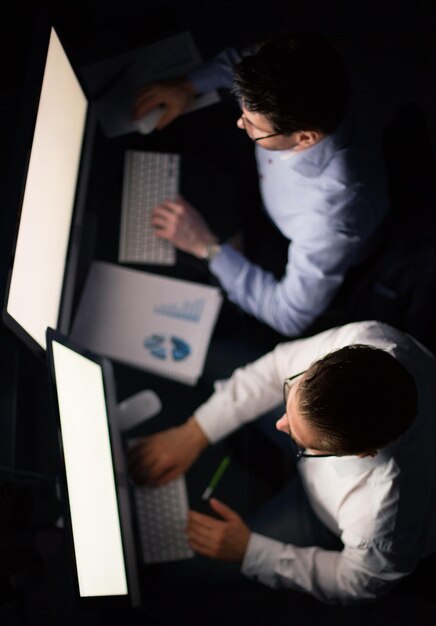 Dos hombres de negocios haciendo un informe financiero por la noche el concepto de horas extras