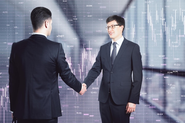Dos hombres de negocios haciendo un trato dándose la mano en el pasillo de la oficina y gráficos de mercado en el fondo Acuerdo y concepto de asociación