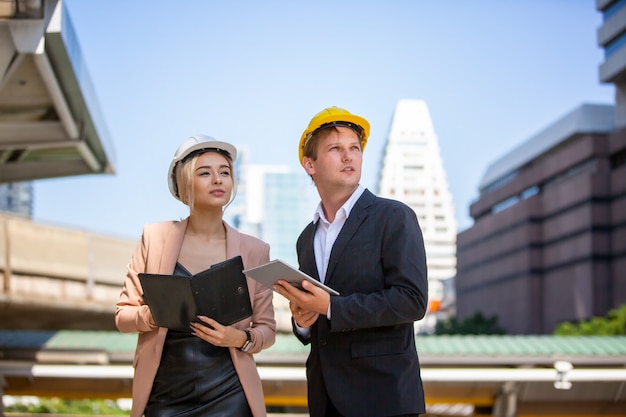 Dos hombres de negocios y mujeres con chalecos de seguridad hablando y apretón de manos en el sitio de construcción