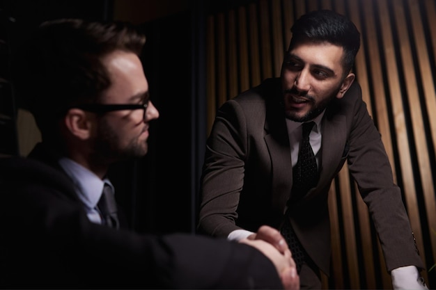 Dos hombres de negocios seguros y positivos estrechando la mano sobre la mesa de reuniones después de la negociación