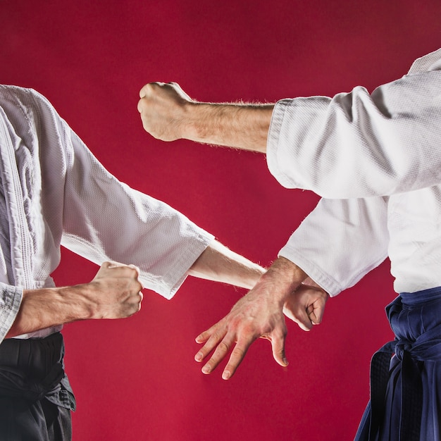 Dos hombres peleando en el entrenamiento de Aikido en la escuela de artes marciales. Concepto de deporte y estilo de vida saludable. Hombres en kimono blanco sobre fondo rojo. Primer plano de manos masculinas sobre fondo rojo studio