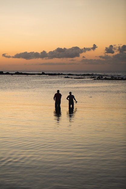 Dos hombres pescando en el océano desde la playa al atardecer