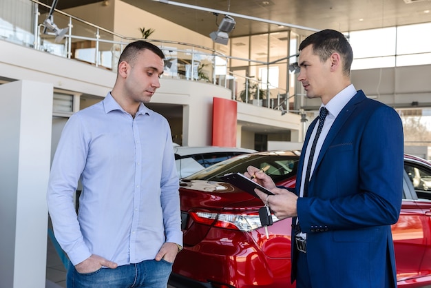 Dos hombres de pie en la sala de exposiciones cerca del coche.