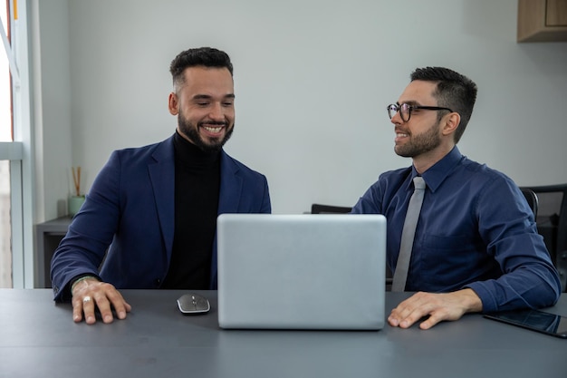 dos hombres sentados en una oficina frente a la computadora sonriendo