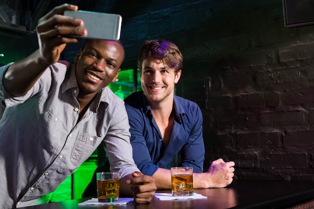 Dos hombres tomando una selfie en el teléfono en barra de bar en bar