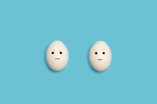 Dos huevos con forma de cara feliz y enojada sobre un fondo azul.