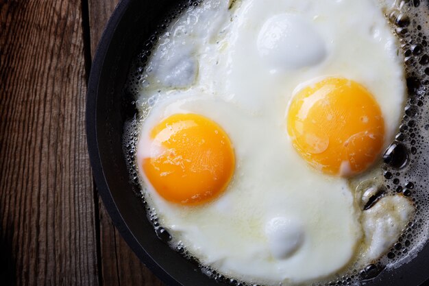 Dos huevos fritos en una sartén de hierro fundido sobre una vieja mesa de madera. Fondo oscuro