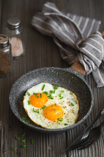 Dos huevos fritos en una sartén pequeña sobre el fondo de madera oscura.