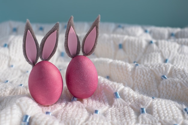 Dos huevos de Pascua rosados con primer plano de orejas de conejo sobre un fondo azul y cuadros de punto blanco. Felices Pascuas