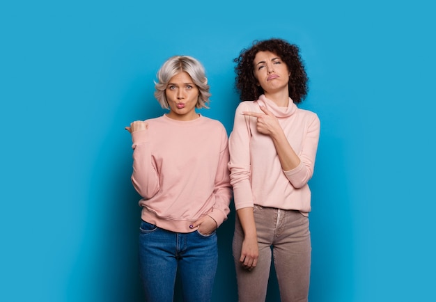 Dos impresionantes mujeres de negocios caucásicas con bonitos cortes de pelo apuntando al espacio de la copia azul están promoviendo algo de confianza