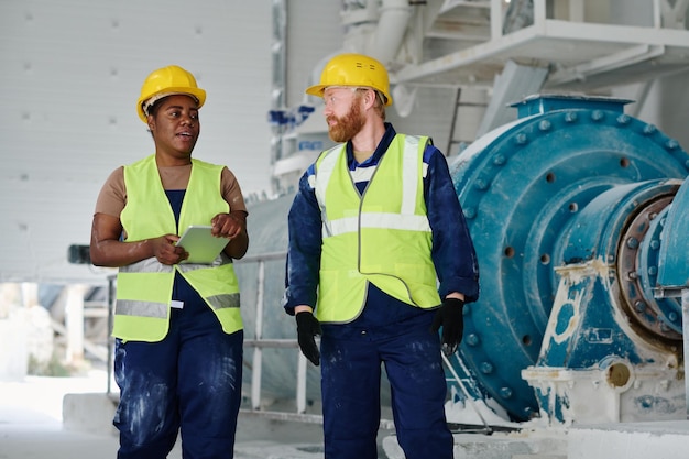 Dos ingenieros confiados en ropa de trabajo y cascos discutiendo puntos de trabajo