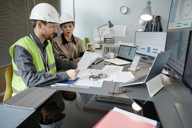 Dos ingenieros diseñando planos en el lugar de trabajo en la oficina y usando cascos