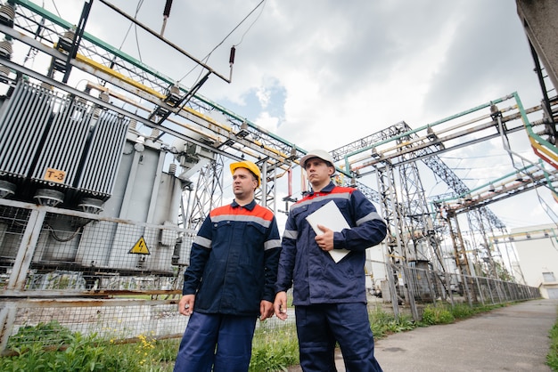 Dos ingenieros especialistas en subestaciones eléctricas inspeccionan equipos modernos de alto voltaje. Energía. Industria.