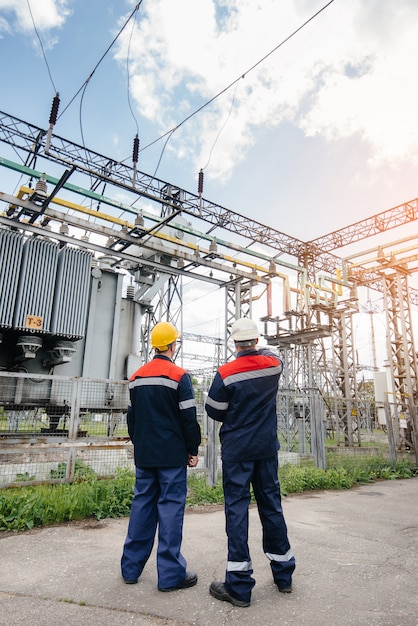 Dos ingenieros especialistas en subestaciones eléctricas inspeccionan equipos modernos de alto voltaje durante la puesta de sol.