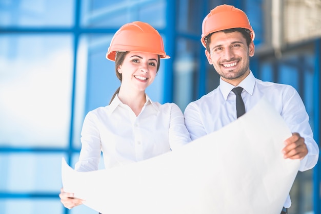 Los dos ingenieros están de pie con un papel sobre el fondo del edificio.