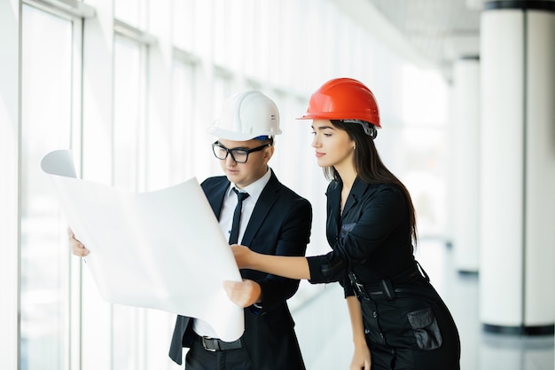 Los dos ingenieros se paran cerca de la ventana panorámica y gesticulan sobre el plan de construcción.