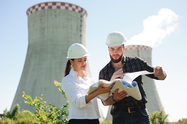 Dos ingenieros de pie en la estación de electricidad, discutiendo el plan.