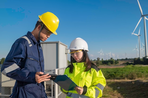 Dos ingenieros que trabajan y sostienen el informe en la estación de generación de energía de la granja de turbinas eólicas en la montaña Gente de Tailandia Técnico hombre y mujer discuten sobre el trabajo