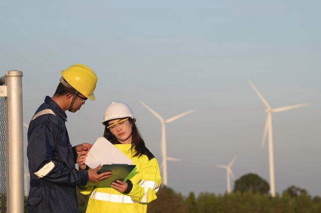 Dos ingenieros que trabajan y sostienen el informe en la estación de generación de energía de la granja de turbinas eólicas en la montaña Gente de Tailandia Técnico hombre y mujer discuten sobre el trabajo