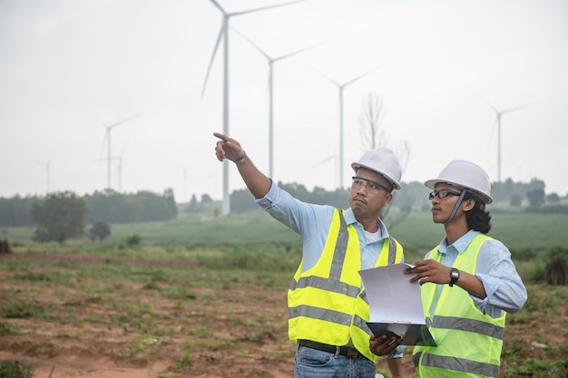 Dos ingenieros que trabajan y sostienen el informe en la estación generadora de energía de la granja de turbinas eólicas en la gente de mountainThailand