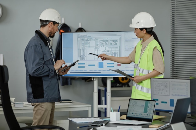 Dos ingenieros revisando planos en el interior y apuntando a la pantalla de la computadora