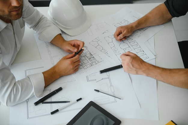 Dos ingenieros trabajando juntos y usando una tableta digital que busca planos y análisis con un plan arquitectónico en el escritorio