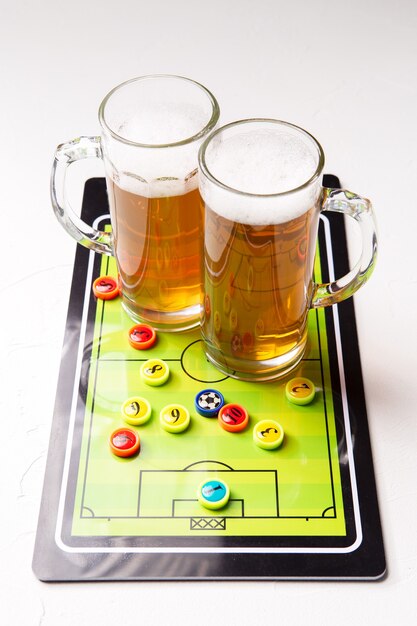 Dos jarras de cerveza espumosa con futbolín en mesa blanca