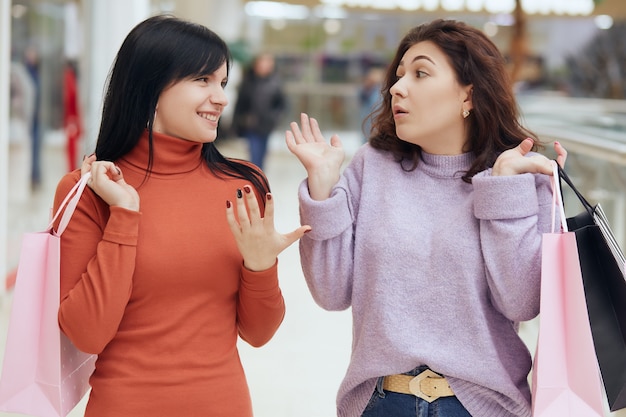 Dos joven vistiendo ropa casual y cabello oscuro, caminando en el centro comercial y cotilleando