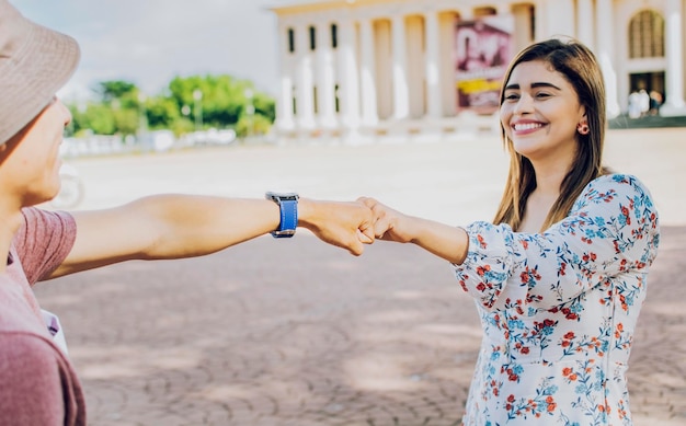 Dos jóvenes adolescentes sonrientes chocando los puños en la calle Cerca de un chico y una chica estrechando los puños en la calle Un chico y una chica dándose la mano en la calle