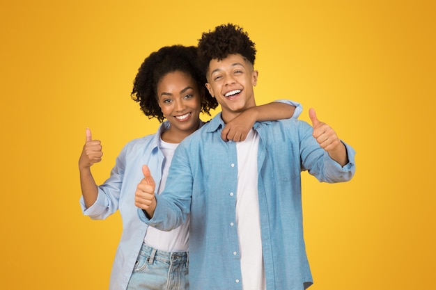 Dos jóvenes adultos alegres levantan el pulgar con entusiasmo hacia la cámara mostrando positividad y aprobación.