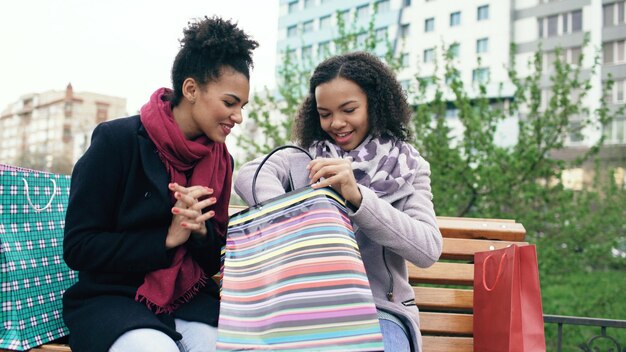 Dos jóvenes afroamericanas compartiendo sus nuevas compras en bolsas de compras entre ellas