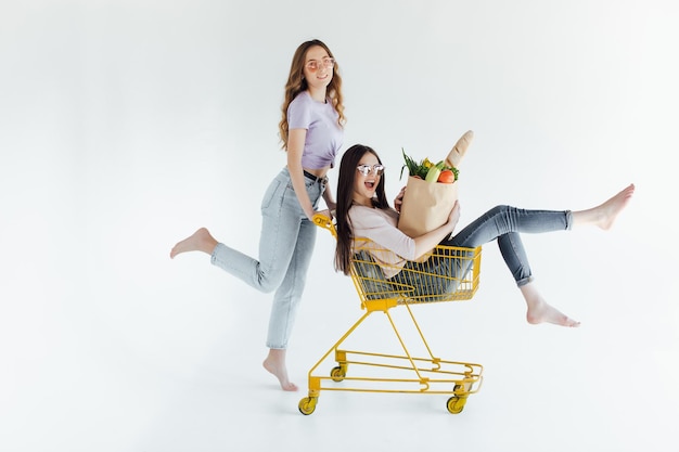 Dos jóvenes alegres con coloridos trajes de moda sonriendo y divirtiéndose con el carrito