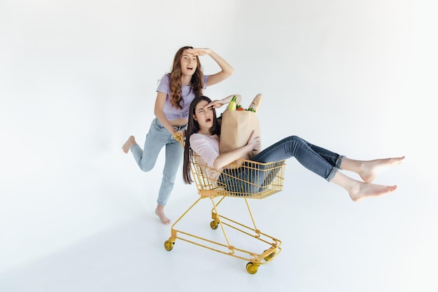 Dos jóvenes alegres con coloridos trajes de moda sonriendo y divirtiéndose con el carrito