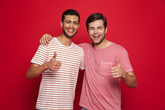 Foto dos jóvenes alegres que se encuentran aisladas sobre la pared roja, dando pulgar hacia arriba