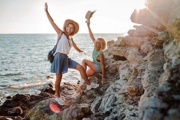 Dos jóvenes alegres con sombreros de hipsters en una roca en la costa del mar