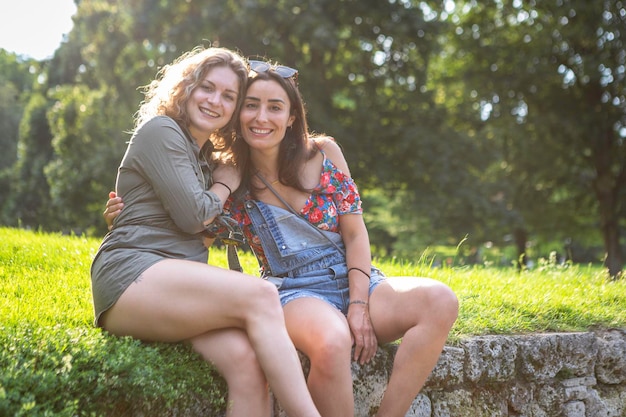 Dos jóvenes alemanas sentadas en una pared sonriendo a la cámara de brazo en brazo