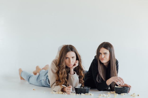 Dos jóvenes amigas bastante alegres que se encuentran aisladas sobre fondo blanco, comiendo palomitas de maíz