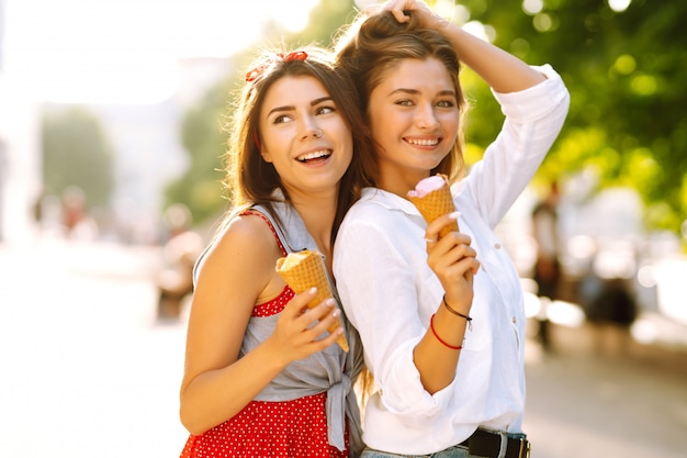 Dos jóvenes amigas divirtiéndose y comiendo helado.