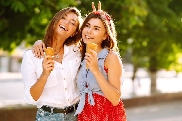 Dos jóvenes amigas divirtiéndose y comiendo helado.