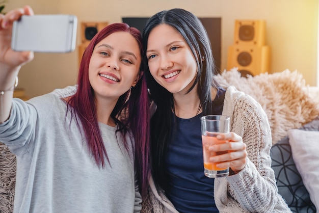 Dos jóvenes amigas felices haciendo selfies mientras se sientan en el sofá en el interior