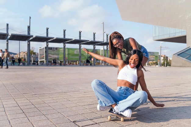 Dos jóvenes amigas negras se ríen divertidas jugando con una patineta, concepto de juventud y amistad, copian espacio para texto