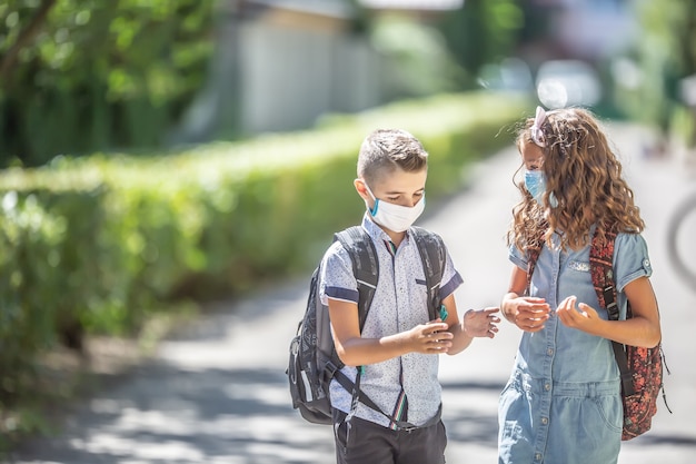 Dos jóvenes amigos compañeros de clase con mascarillas hablan de camino a la escuela durante la cuarentena de Covid-19.