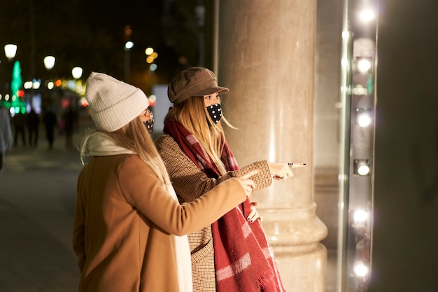 Dos jóvenes amigos mirando en un escaparate, en una ciudad de noche. Apuntan a algo en la tienda.