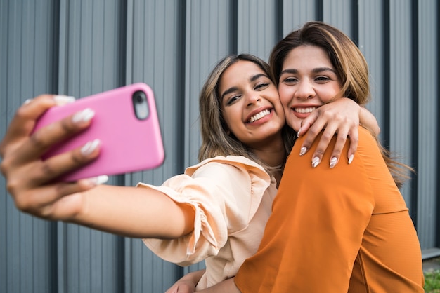 Dos jóvenes amigos sonriendo y tomando un selfie con su teléfono móvil mientras están de pie al aire libre