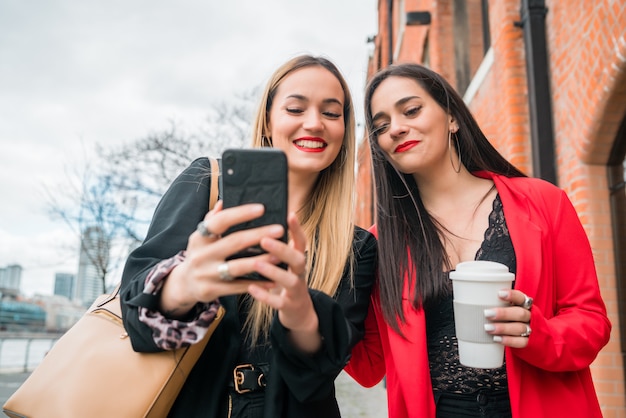 Dos jóvenes amigos usando su teléfono móvil al aire libre.