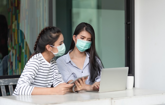 Dos jóvenes asiáticas con máscara médica para proteger el coronavirus o la enfermedad COVID-19 mientras trabajan en el exterior