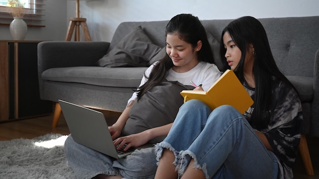 Dos jóvenes asiáticas sentadas en el suelo y navegando por internet con una computadora portátil