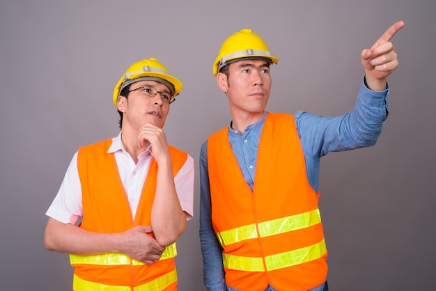 Dos jóvenes asiáticos, trabajador de la construcción juntos contra la pared gris